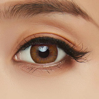 A close-up of a brown eye with long lashes and a groomed brow, enhanced by Acuvue Define Fresh Honey (30pk) lenses from Acuvue, revealing detailed iris patterns and subtle eyelid makeup.