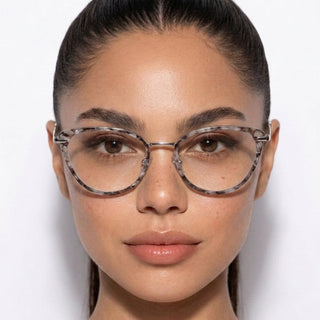 A woman with smooth, medium-toned skin and dark hair pulled back models EyeCandys Aura Cat Eye eyewear, featuring a wide fit and round tortoiseshell style. She faces the camera directly against a white background.
