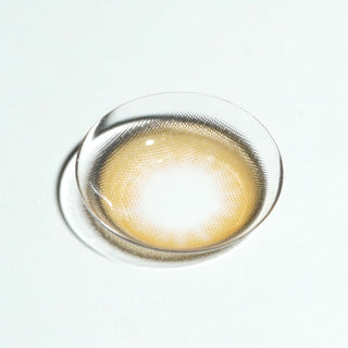 The EyeCandys Pink Label Barcelona Brown contact lens, featuring a light center and dark rim, is displayed on a white surface—ideal for anyone wanting natural-looking brown contacts.