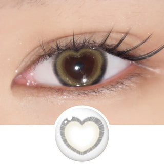 Close-up of eye with long lashes wearing EyeCandys Brown Heart contact lens – beige-brown heart-shaped design floats on the iris, giving subtle enlargement, natural coverage, and a warm, romantic sparkle. Lens design shown below.