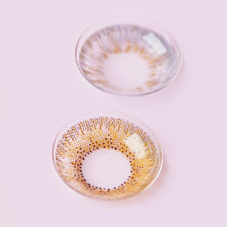 Two colour contact lenses (brown and grey with limbal ring designs) photographed on a pink background