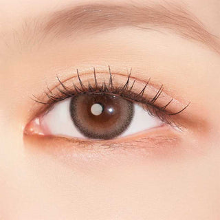 Model with brown eyes wearing EyeCandys Clalen Mimosa Brown Oversea prescription contact lenses, featuring a warm brown color with a subtle, natural look. These lenses offer a comfortable, all-day wear experience, enhancing the eyes with a beautiful, defined appearance