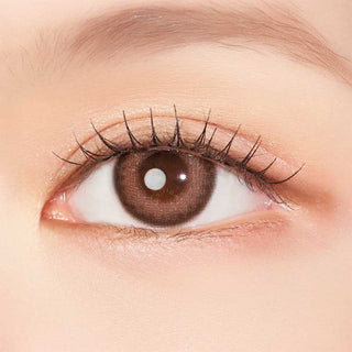 A close-up of a human eye with a light brown iris, long curled lashes, and natural makeup highlights the subtle effect of Clalen IRIS Pink Tulip (10pk) colored contacts by Clalen, suitable even for myopia prescriptions.