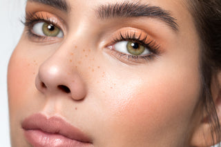 Model wearing Glossy Ivory natural colored contact lenses on top of dark brown irises with natural curled lashes and peach eyeshadow