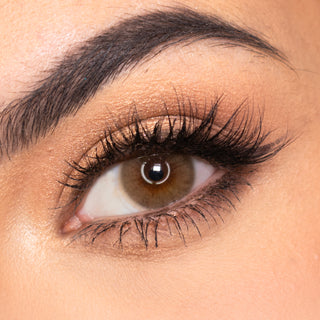 Model with natural dark brown eyes, wispy lashes, and beautiful eyebrows, wearing EyeCandys Glossy Hazel prescription colored contact lens. The lenses enhance her natural eye color with a warm, hazel tone, providing a subtle and vibrant look.