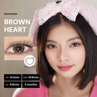 Model’s face wearing EyeCandys Brown Heart contact lens – beige-brown heart-shaped design floats on the iris, giving subtle enlargement and natural coverage. Lens specifications: Diameter 14.1 mm, Graphic Diameter 13.6 mm, Base Curve 8.6, Water Content 38%, Replacement Cycle 3 months.