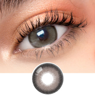 Close-up photo displaying the Toronto Grey contact lens on a white background, worn by a model with dark brown eyes and subtle eye makeup, including peach eyeshadow. The image also highlights a cutout of the contact lens.