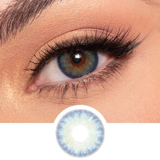 Blue multi-tone contact lens (EyeCandys Isla Blue Grotto) worn on a brown eye with neutral eye makeup and wispy eyelashes, above the eye contact design on a white background.
