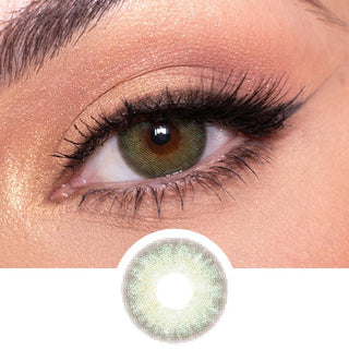 Close-up of a person's eye with dreamy EyeCandys Isla Set (3 Pairs) contact lenses in a vibrant green shade. The person has a well-defined eyebrow, shimmery eye shadow, and long, dark eyelashes. Below the eye is an enlarged image of the colored contact lens design, reminiscent of tropical paradises.