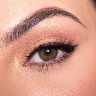 Close-up shot of a model wearing EyeCandys Isla Emerald Green colored contact lens in one eye that is naturally dark-brown