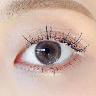 Close-up shot of model's eye adorned with Chuu Milk & Tea Cream Grey color contact lenses with prescription, complemented by minimalist eye makeup, showing the brightening and enlarging effect of the circle contact lens on dark brown eyes.