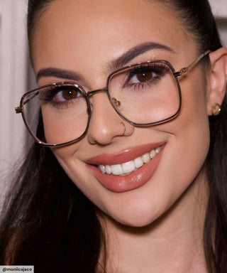 Model with black hair and natural simple make up look wearing Mystic Oversized Square vintage-inspired prescription eyeglasses, available in blue light blocking lenses and in readers with magnification, from EyeCandys. Pictured is the Smoke Crystal (silver-grey) color.