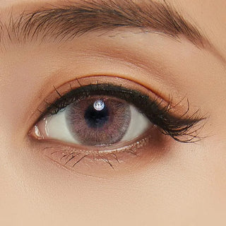 A close-up of an eye with light brown skin, long lashes, a defined eyebrow, and NEO Vision Cosmo Brown prescription contacts by NEO Vision. The eyelid shows natural eyeshadow and the smooth skin appears well-lit.