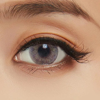 A close-up of a person's eye wearing NEO Vision Cosmo Grey lenses by NEO Vision, with a groomed eyebrow, long lashes, and natural makeup.