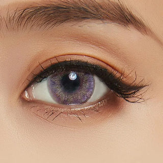 A close-up of a person's eye wearing NEO Vision Cosmo Violet circle lenses by NEO Vision, featuring long eyelashes, a neatly groomed eyebrow, and subtle eyeshadow makeup.
