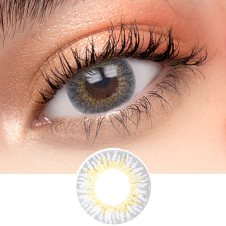 Close-up of Pink Label New York Grey contact lens on a white surface with a model displaying dark brown eyes, complemented by natural eye makeup, beside a cutout of the contact lens.