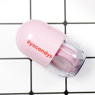 A small, cylindrical pink Pill-Shaped Contact Lens Case Kit with the brand "EyeCandys" printed in red letters. The clear bottom half reveals contact lens holders inside. Soft-tipped tweezers are included for easy handling. It's placed on a white and black grid surface, making it both practical and stylish.