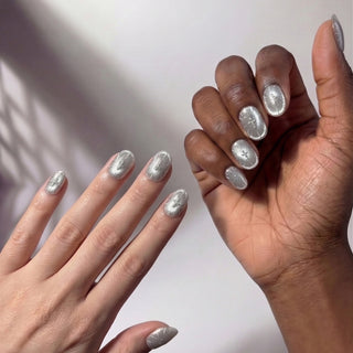 Hand wearing EyeCandys Cygnus press on nails featuring ice grey cat eye base with silver metallic cross details in a modern short almond shape.