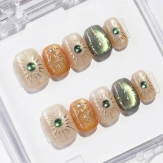 Close-up of EyeCandys Sun Spell press on nails with cat-eye finish in nude, amber, and green shades featuring sun motif details on a white background.