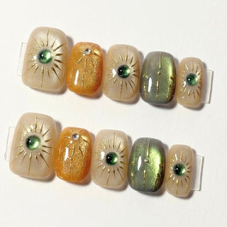 EyeCandys Sun Spell press on nails featuring a mixed cat-eye set in nude, amber, and green with hand-drawn sun details, artistic and summery design.