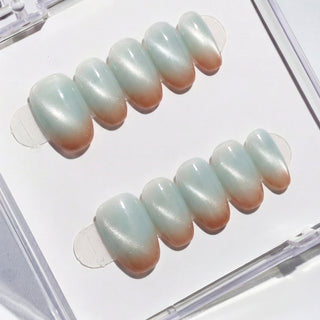 Close-up of EyeCandys Blue Hour Latte press on nails featuring a milky blue glassy base with soft cat-eye shimmer and subtle brown gradient tips on a white background.