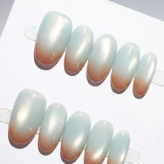 Close-up of EyeCandys Blue Hour Latte press on nails on a white background featuring milky glassy blue base with soft cat-eye glow and subtle chocolate brown gradient tips.