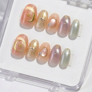 Close-up of EyeCandys Star Script press on nails featuring a sunset cat-eye gradient in peach, blush, and gold tones with metallic star and symbol details on a white background.