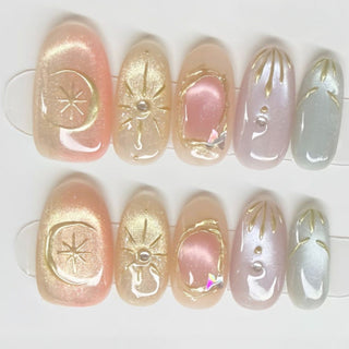 Close-up of EyeCandys Star Script press on nails on a white background featuring warm sunset cat-eye gradient in peach, blush, and muted gold with sculpted gold star and celestial motifs.