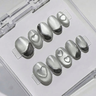 Close-up of EyeCandys Soft Signals press on nails featuring smooth grey cat-eye base with magnetic shimmer, silver chrome curves, and subtle sculpted heart accents on a white background.