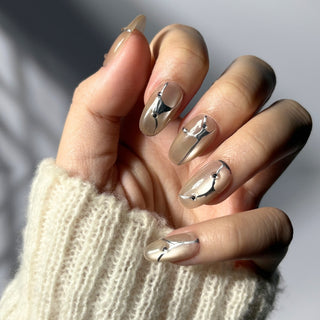 Hand showcasing EyeCandys In the Lines press on nails featuring white cat-eye shimmer with delicate silver line detailing and gem accents.