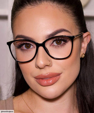 Model with black hair and natural simple make up look wearing Peggy Oval vintage-inspired prescription eyeglasses, available in blue light blocking lenses and in readers with magnification, from EyeCandys. Pictured is the Black Gold color.