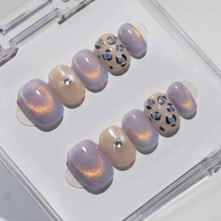EyeCandys' Purr-ple Reign Press-On Nails feature handmade gel nails in soft lavender and beige with glitter, metallic accents, and leopard prints—neatly arranged in a clear case for a salon gel manicure look.
