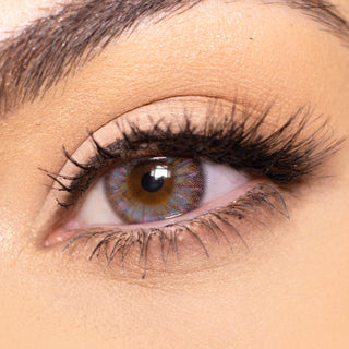Close-up shot of a model eye wearing multi-tone Brown Violet colored contact lens in one eye that is naturally dark-brown with natural eye make up