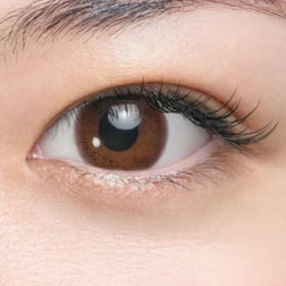 Close-up of eye wearing EyeCandys Seed Coffret Sweetie Make Brown (10pk) prescription colored contact lens, warm brown iris with pink undertone, floral pattern and glossy finish, natural Korean daily disposable contact lens for dark eyes