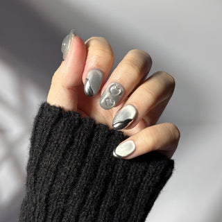 Hand showcasing EyeCandys Soft Signals press on nails featuring smooth grey cat-eye finish with metallic silver accents and sculpted hearts.