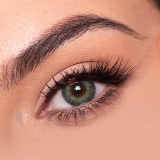 Close-up shot of a model eye wearing Sugarlook green colored contact lens in one eye that is naturally dark-brown with natural eye make up