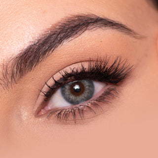 Close-up shot of a model eye wearing Sugarlook grey colored contact lens in one eye that is naturally dark-brown with natural eye make up