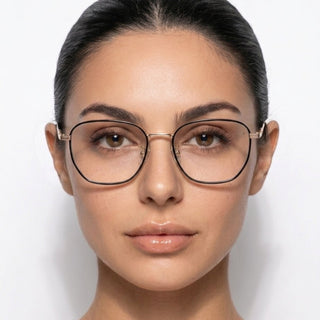A woman with dark hair pulled back wears EyeCandys Therese Oversized Square gold-rimmed eyewear, looking directly at the camera with a neutral expression against a plain white background.