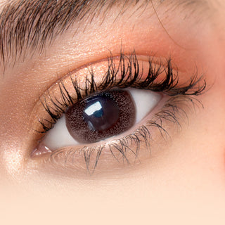 Close-up of model showcasing Toronto Grey contact lenses over dark brown irises, complemented by naturally curled lashes and peach eyeshadow