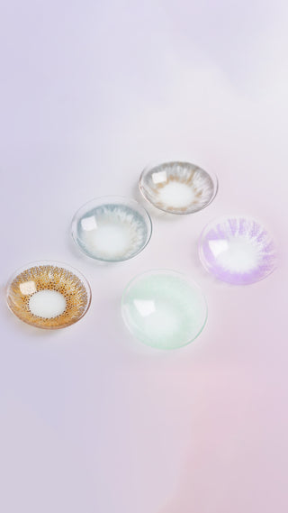 Various color contact lenses in blue, grey, violet, brown and pink, photographed on a purple background