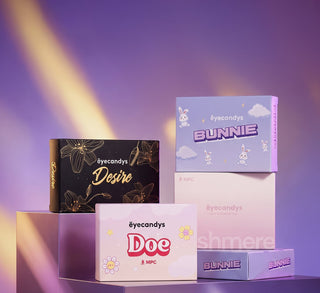 EyeCandys contact lens boxes in Bunnie, Doe, Desire, and Cashmere designs arranged against a dreamy purple backdrop with warm diagonal lighting.