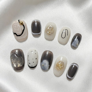 EyeCandys Concrete Poetry press on nails featuring cream and charcoal abstract nails with rose gold contour lines, ink wash design, and gold foil rosette accents.