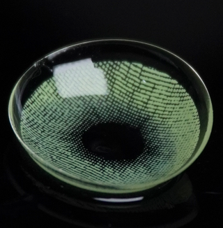 Macro shot of the EyeCandys Dare to be green prescription colored contact lens on a dark background, showing the detailed pattern of the contact lens design