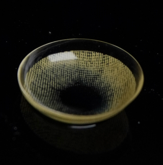 Macro shot of the EyeCandys Dare to be Hazel prescription colored contact lens on a dark background, showing the detailed pattern of the contact lens design