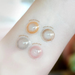 The EyeCandys Attitude Glitter Grey contacts, along with Attitude Brown, Choco, and Pink shades, are shown on a person’s inner forearm, featuring the brand’s natural colored lens collection.