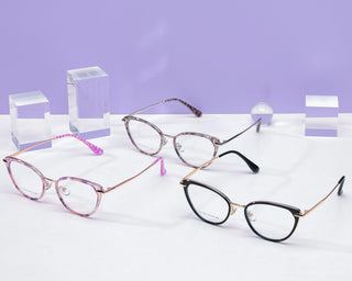 Three EyeCandys Aura Cat Eye eyeglasses in pink, brown, and black are displayed on a white surface with clear acrylic blocks and a small sphere, set against a light purple background.