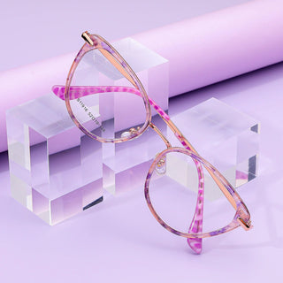 EyeCandys Aura Cat Eye glasses in pink and purple are showcased on clear acrylic blocks with a pastel purple backdrop, featuring a wide fit, translucent cat-eye frame, and subtle pattern on the arms.