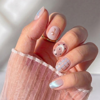 Hand wearing Eyecandys Charmed, I'm Sure press-on nails with a glossy nude pink base, whimsical mixed nail art, and a salon-quality short round shape.
