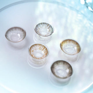 Macro shot of various circle contact lenses in shades of grey, brown and chocolate, on a light blue background