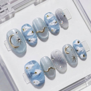 Short oval press on nails Gilded Cirrus with impressionist sky blue tones, soft cloud artwork, and gold celestial moon and star accents.